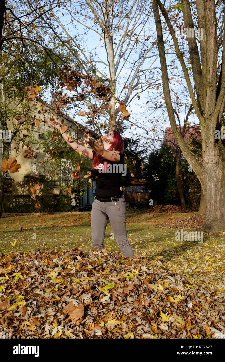 Jeune femme de jeter les feuilles en l'air dans un parc lenti Hongrie Zala County Banque D'Images