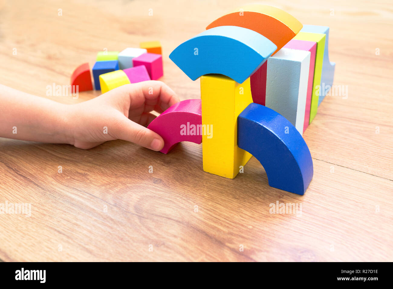 Un enfant joue avec des blocs de couleur, les cubes colorés construit un modèle sur un fond de bois foncé Banque D'Images