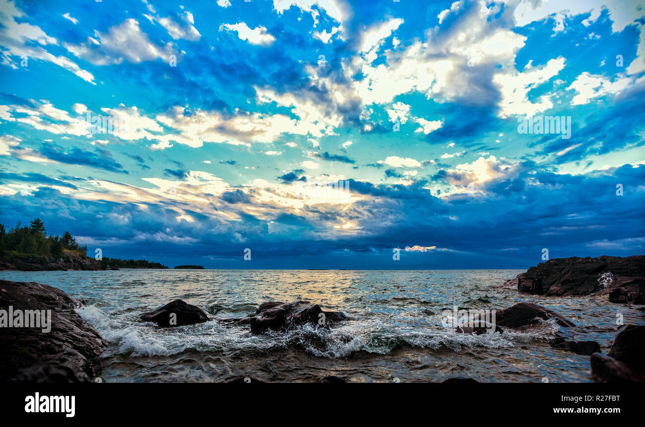 Confettis brillants nuages Lakeshore. Nuages colorés le ciel bleu au-dessus d'un éperon rive du lac Supérieur. Seascape background with copy space. Banque D'Images