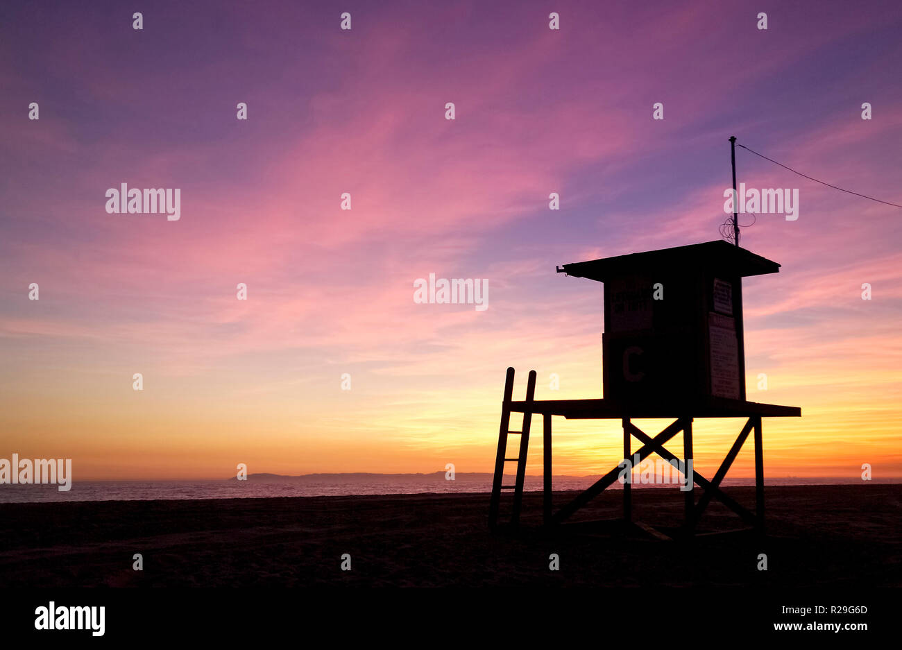 Une station de sauvetage à la fin de la journée se profile comme le coucher de soleil sur l'île de Catalina et l'océan Pacifique à Newport Beach en Californie du Sud, aux États-Unis. Banque D'Images