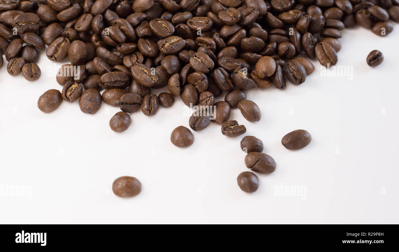 Brown, grains de café torréfiés sont montré de près et lâchement étalés sur une plaine, surface blanche. Banque D'Images