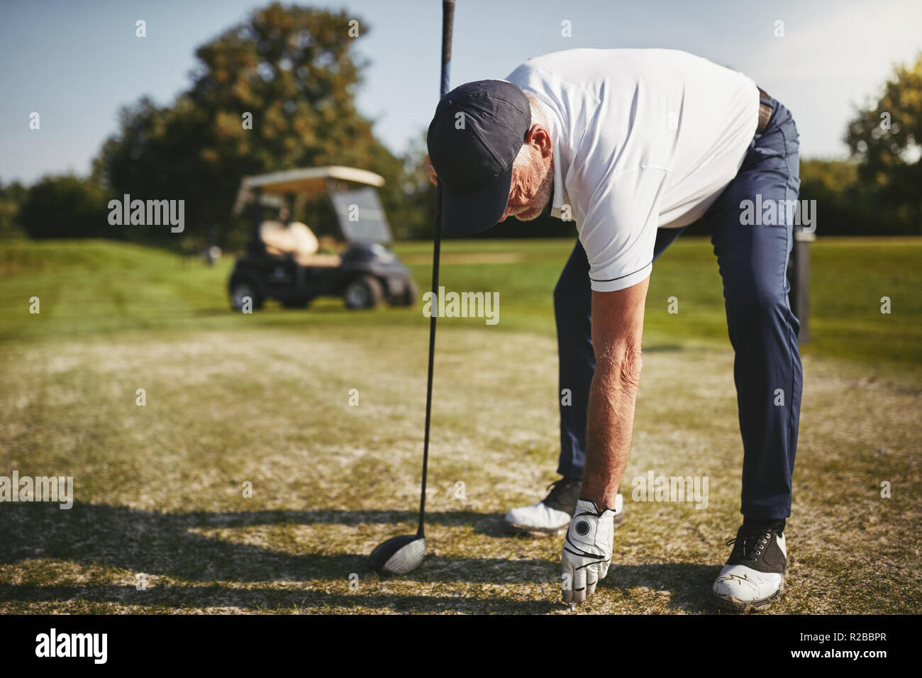 Sporty man plaçant une balle sur un tee en jouant une partie de golf sur une journée ensoleillée Banque D'Images