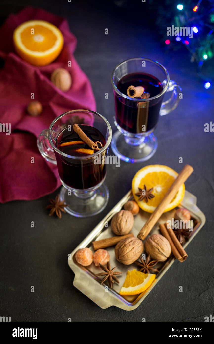 Composition d'hiver. Du vin rouge dans des verres à fond noir. Couronne de sapin, l'éclairage électrique, plateau avec l'orange, la cannelle, noix et épices, rouge n Banque D'Images