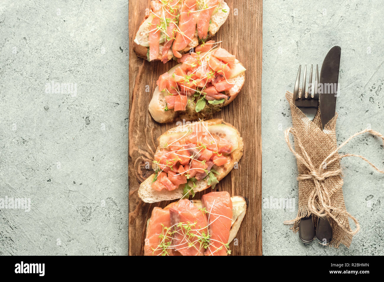 Bruschetta de tranches de saumon poisson, concombre, roquette et les jeunes pousses d'herbe sur une carte de cuisine pour servir sur fond gris servi avec un couteau un Banque D'Images