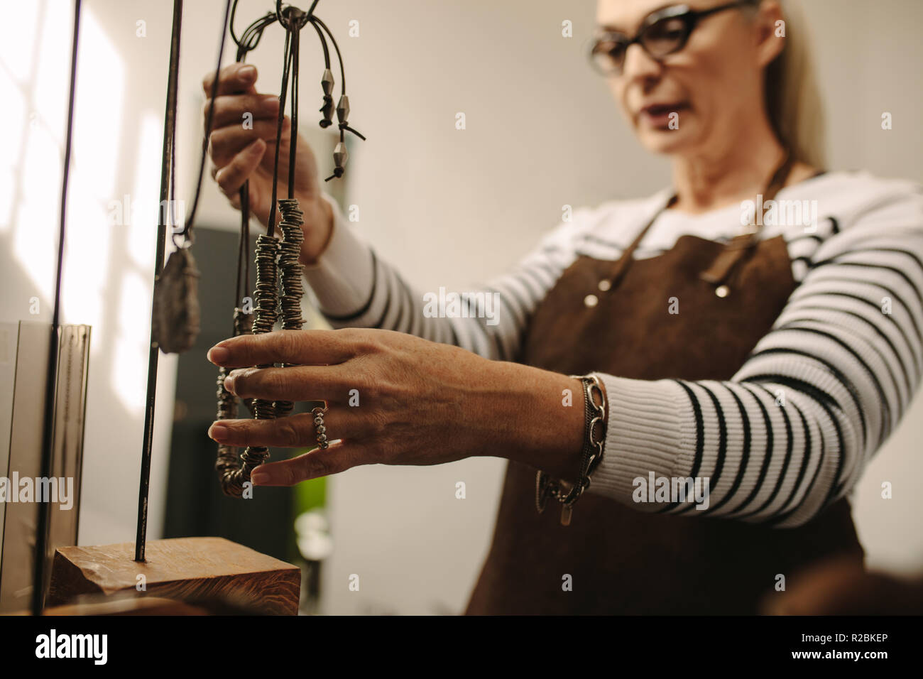 Femelle adulte pendaison bijoutier un collier sur support. Female woman goldsmith travaillant à son studio de design. Se concentrer sur les mains avec des bijoux. Banque D'Images