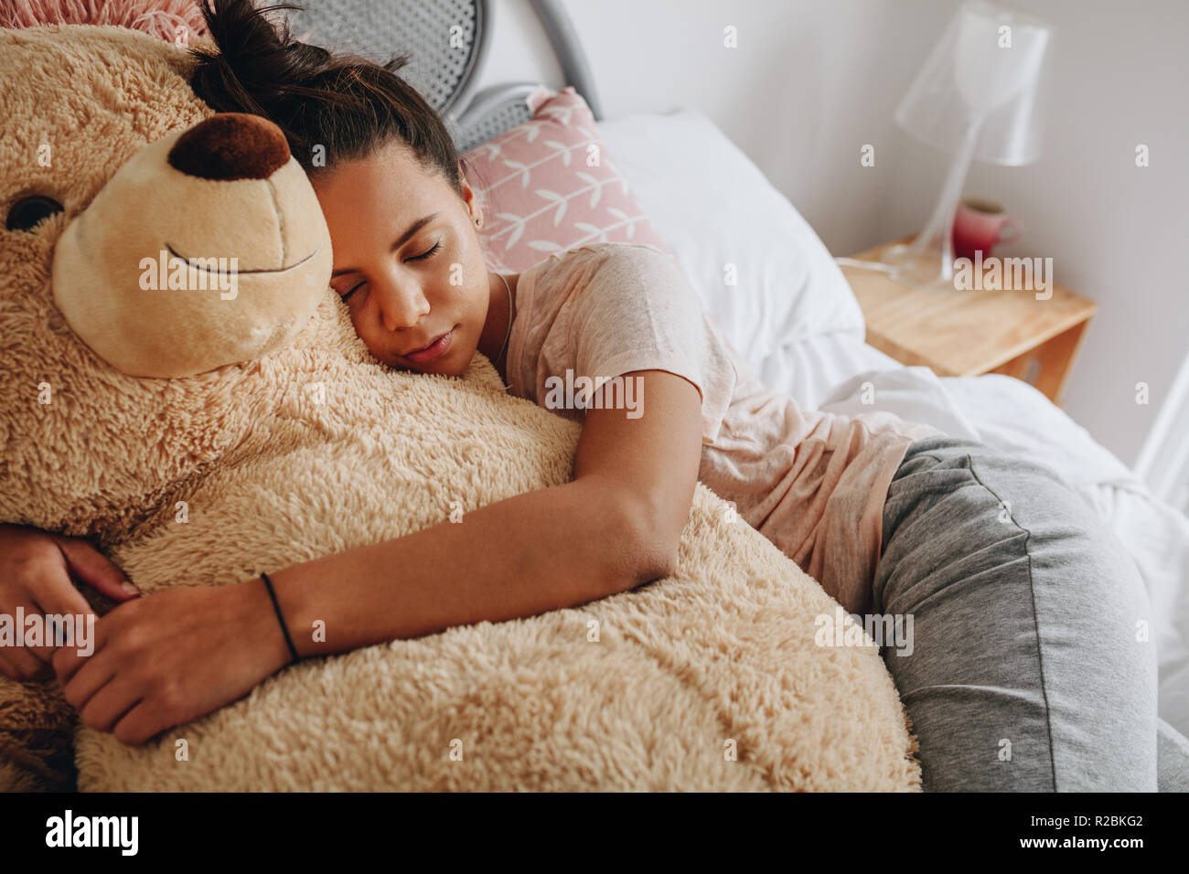 Jeune fille dormir avec ses bras autour d'un grand ours en peluche sur le lit. Girl sleeping on bed serrant un ours en peluche brun. Banque D'Images