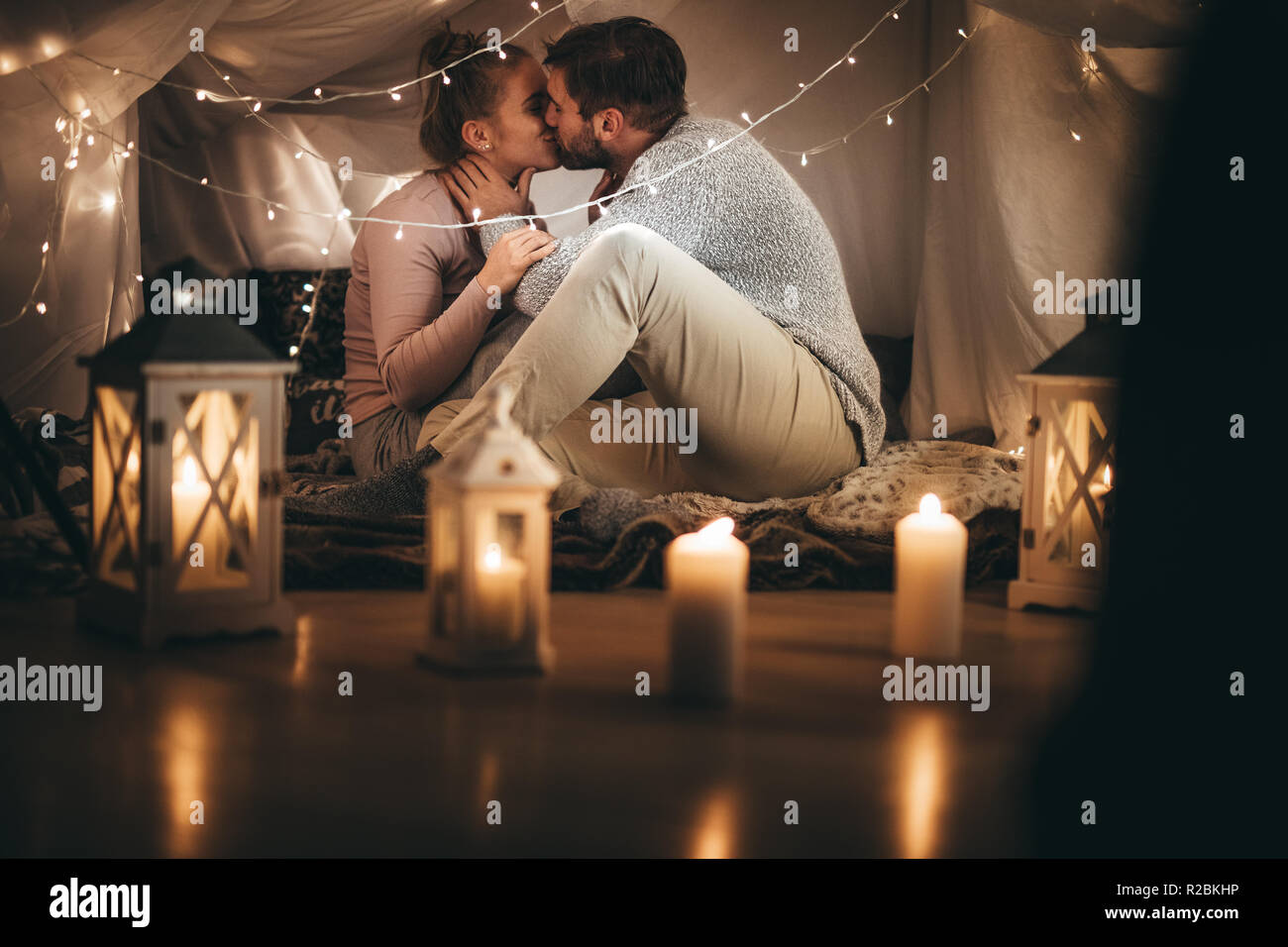 Couple romantique à la maison assis sur le même lit le soir avec des bougies  allumées dans la salle. L'homme s'embrasser sa femme assis sur le lit  décoré de petits serial Photo