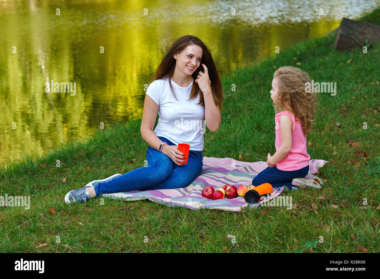 Pique-nique en famille. Mère et fille s'asseoir sur la couverture pour le  bord de la rivière. Petite fille et sa mère s'agit. Les pommes sont  allongés sur une couverture. De temps ensemble