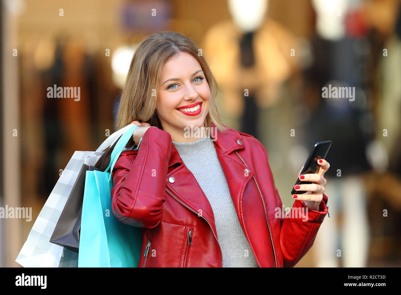 Happy shopper holding shopping bags et smart phone looking at camera dans un centre commercial Banque D'Images