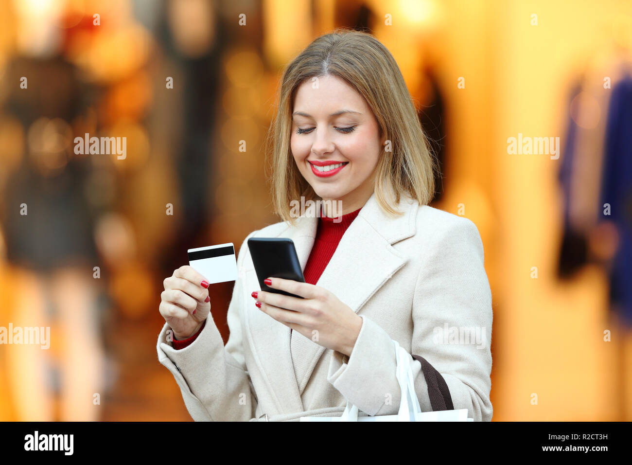 Happy woman acheter en ligne avec carte de crédit et smart phone dans la rue d'un centre commercial en hiver Banque D'Images
