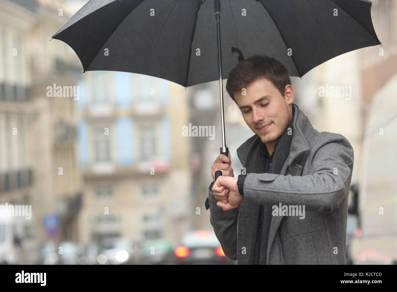 Man checking smartwatch sous la pluie marcher dans la rue en hiver Banque D'Images