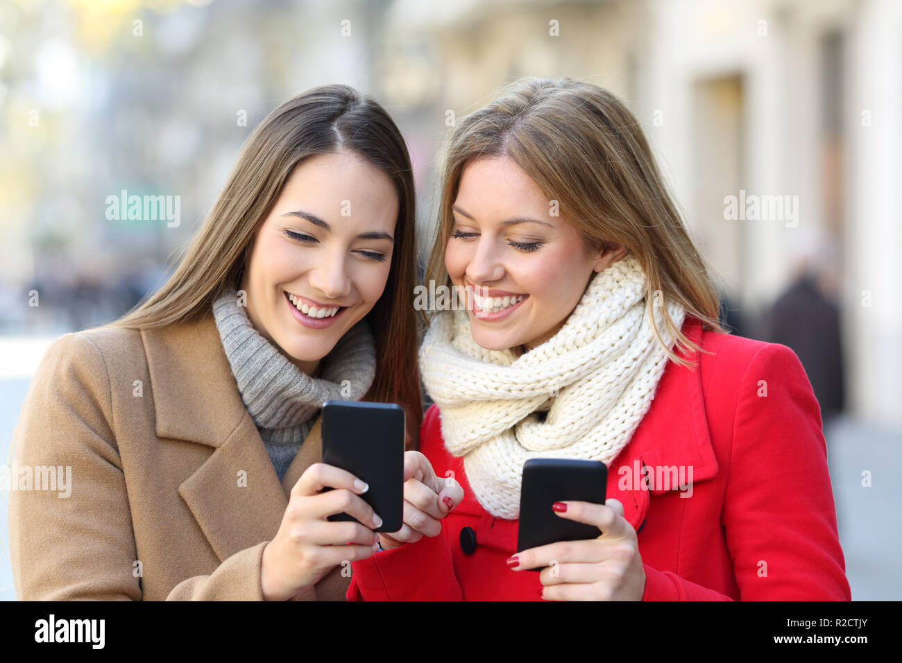 Les amis consulting smart phone content dans la rue en hiver Banque D'Images