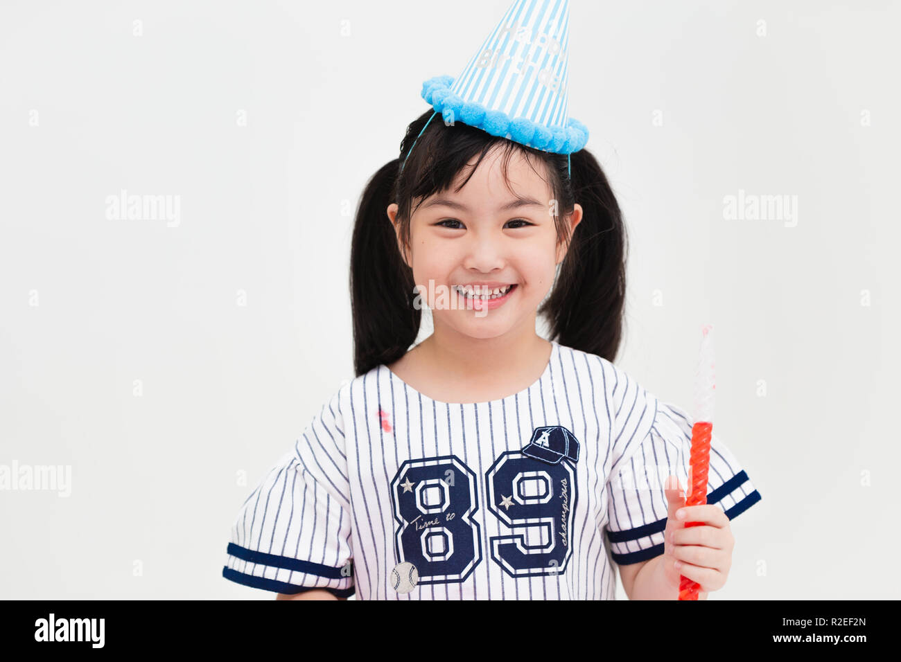 Cute Asian girl child in party hat avec sweet candy isolated on white background studio. Banque D'Images