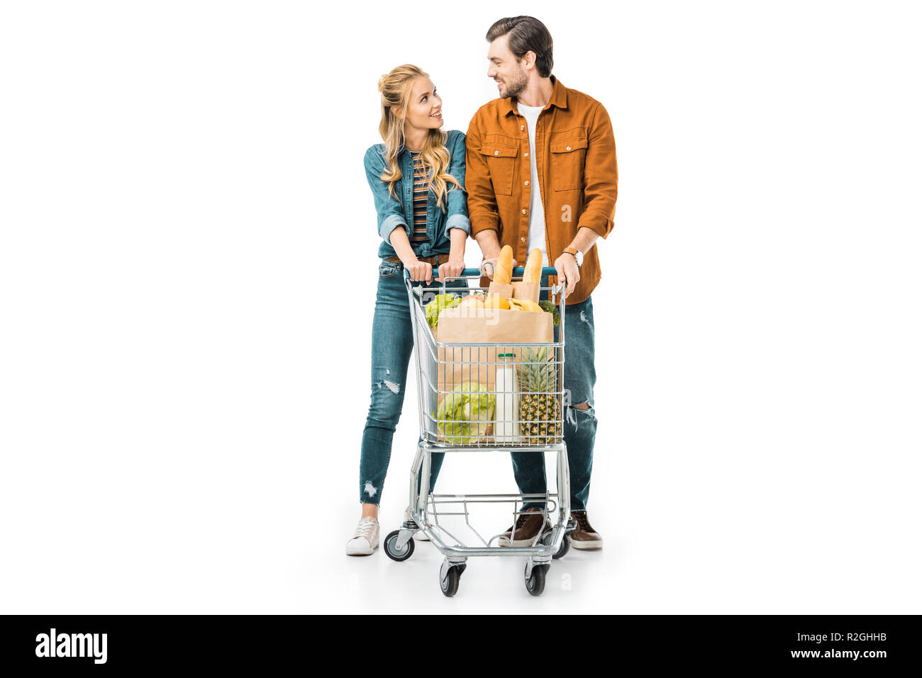 Heureux couple carrying shopping trolley avec des produits et à la recherche à chaque autre isolated on white Banque D'Images