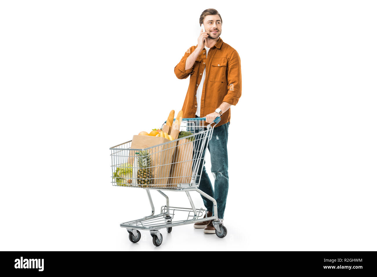 Cheerful man carrying shopping trolley avec des produits dans des sacs en papier et de parler sur smartphone isolated on white Banque D'Images