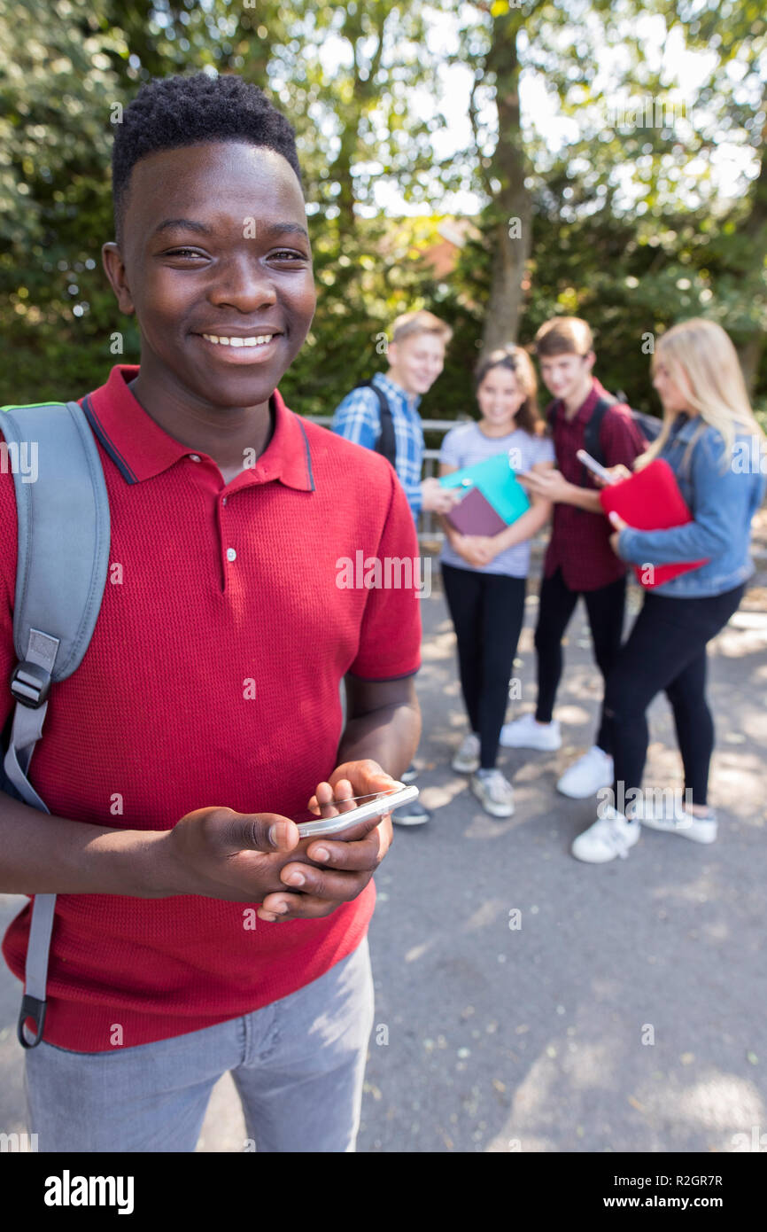 Portrait d'homme élève de l'École des adolescentes en plein air avec des amis Holding Mobile Phone Banque D'Images