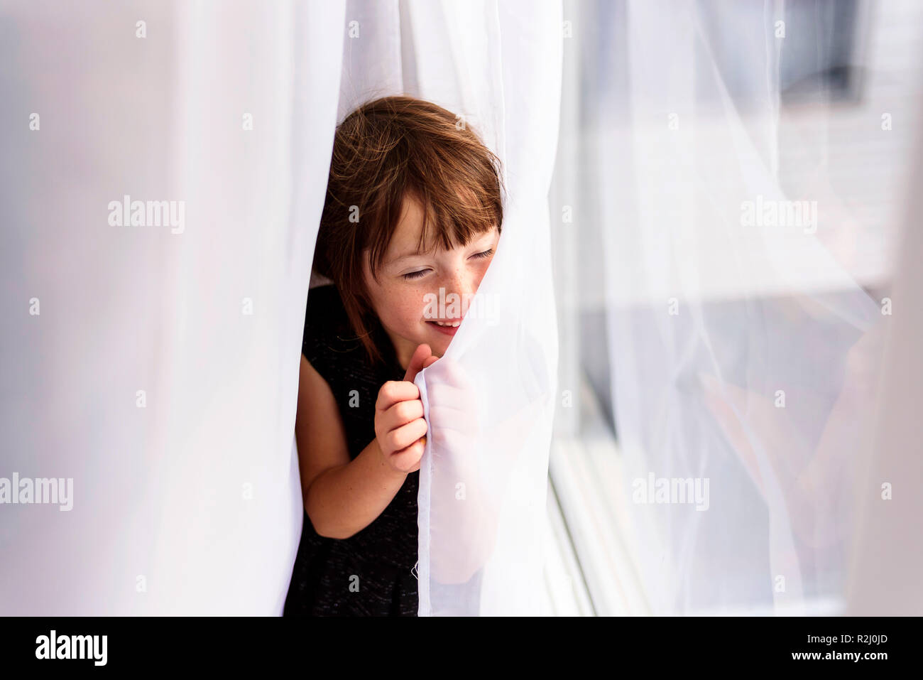 Smiling girl se cachant derrière un rideau Banque D'Images