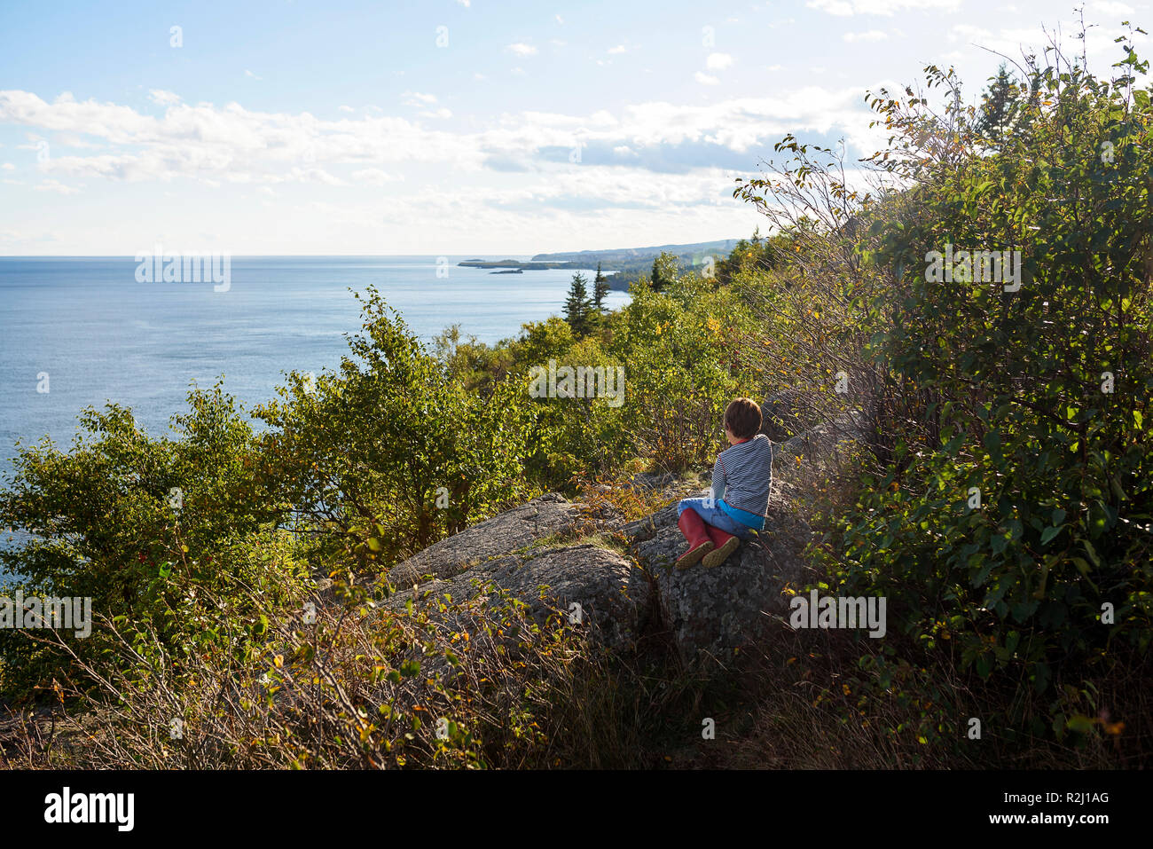 Garçon assis sur les rochers par le lac Supérieur, United States Banque D'Images