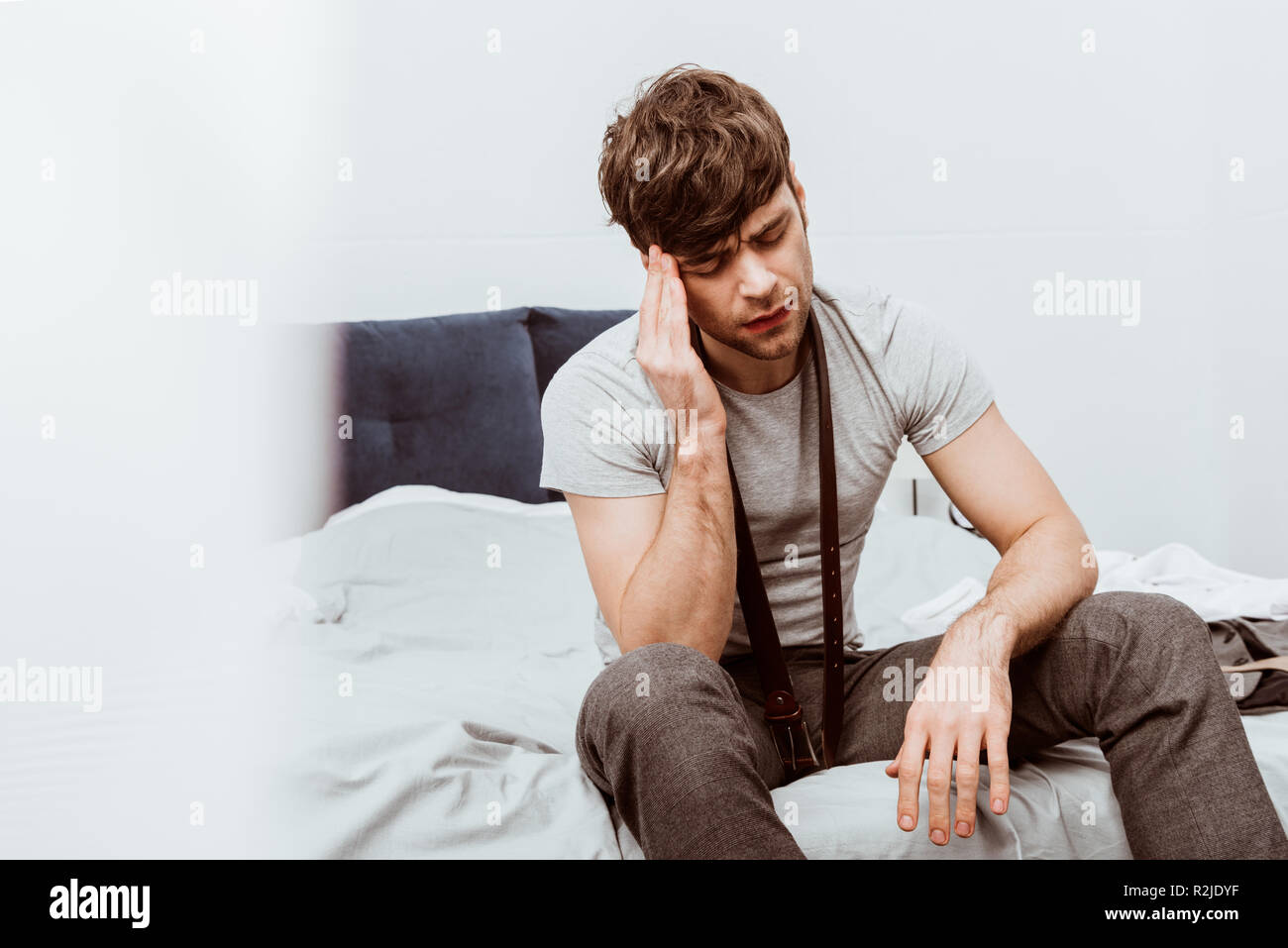 Beau jeune homme avec ceinture sur cou assis sur le lit et avoir des maux  de tête à la maison Photo Stock - Alamy