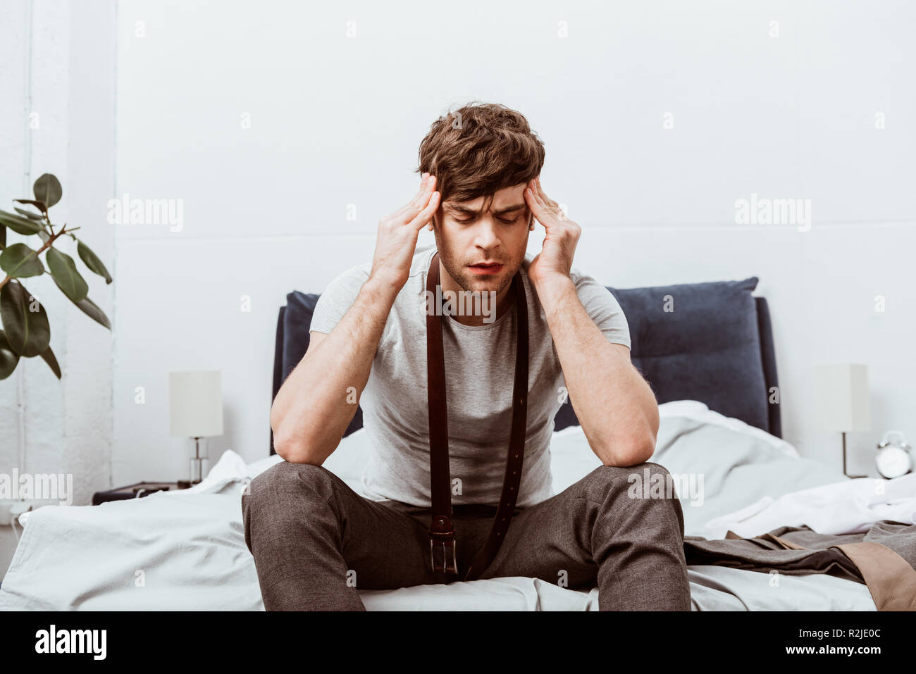 Jeune homme avec ceinture sur cou assis sur le lit et avoir des maux de  tête à la maison Photo Stock - Alamy