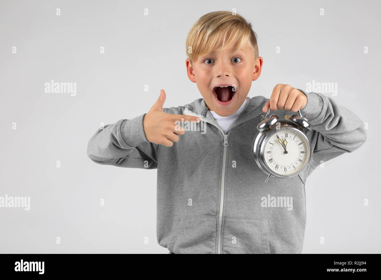 Petit garçon blond a un réveil et elle s'étonne, montre son grand temps avec la bouche ouverte. Banque D'Images