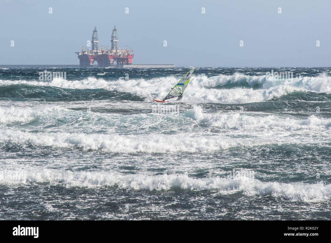 Planche unique dans la baie de Medano Tenerife au large de la côte de l'équitation dans de forts vents à travers les vagues. Dans l'arrière-plan du port avec deux appareils. Banque D'Images