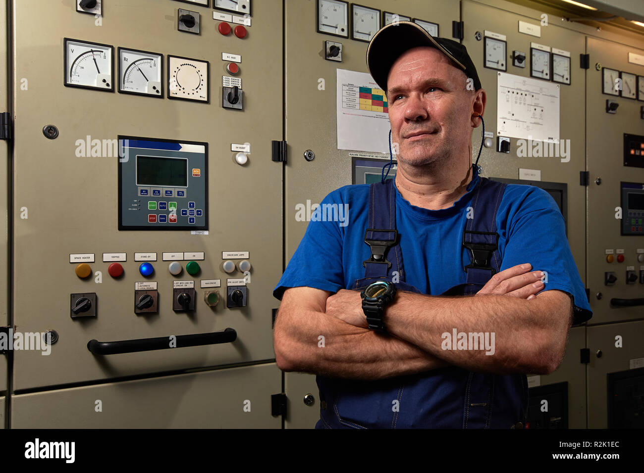 Fier et heureux / mécanicien chef mécanicien, qui posent avec les bras croisés, souriant, enfilé en uniforme dans la salle des machines d'un navire de charge. Banque D'Images