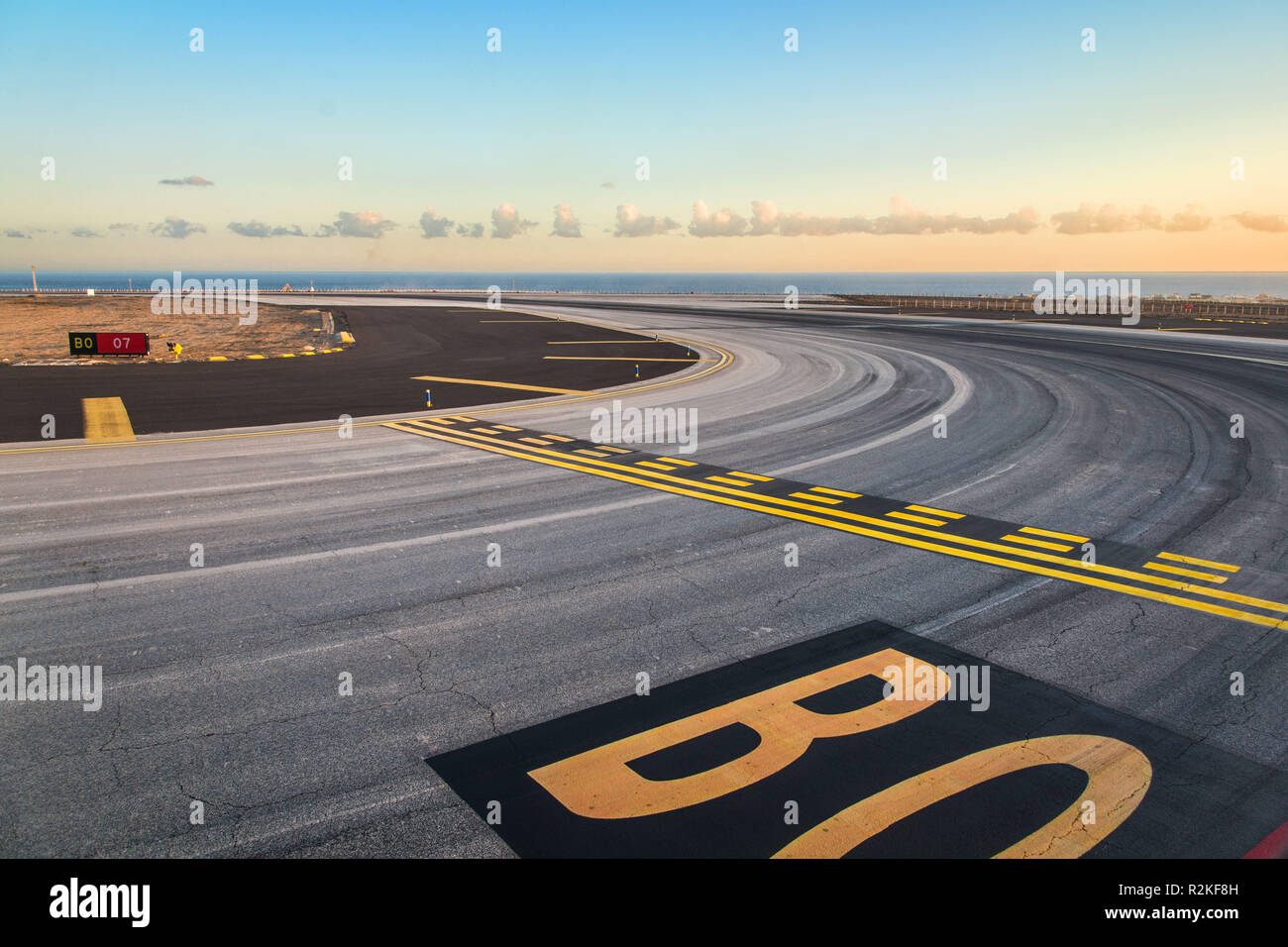 Marques sur la piste d'un aéroport avec ligne d'horizon formée par l'océan et un ciel du soir. Banque D'Images