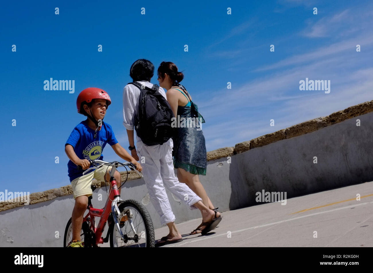 Un jeune garçon sur un vélo au soleil avec crash hat, casque sur par la côte espagnole. Banque D'Images