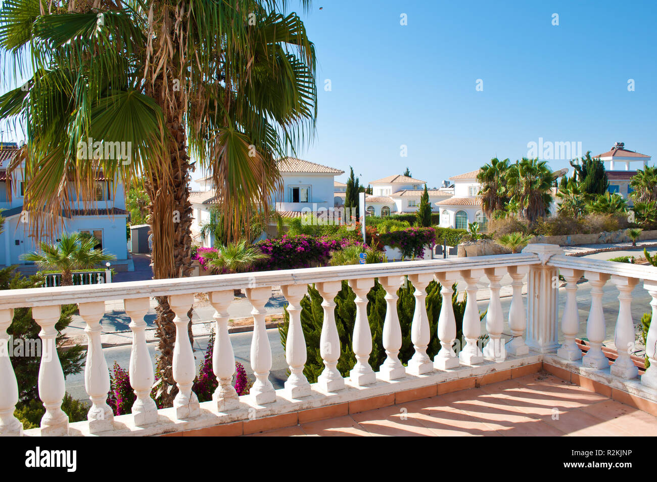 Vue sur une rue avec de nombreuses villas blanches, l'un des palmiers, buissons verts, fleurs roses et feuillage luxuriant derrière un balcon et d'une rampe. Personne n'outsi Banque D'Images