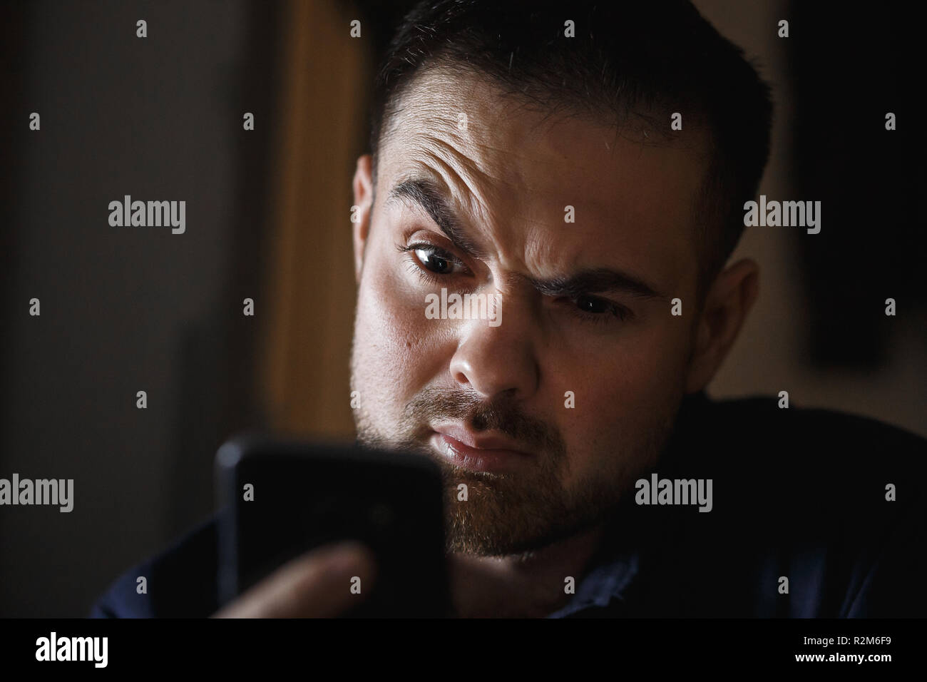 Homme d'âge moyen amazedly barbu à la recherche vers le smartphone dans la chambre noire. Close up. Banque D'Images