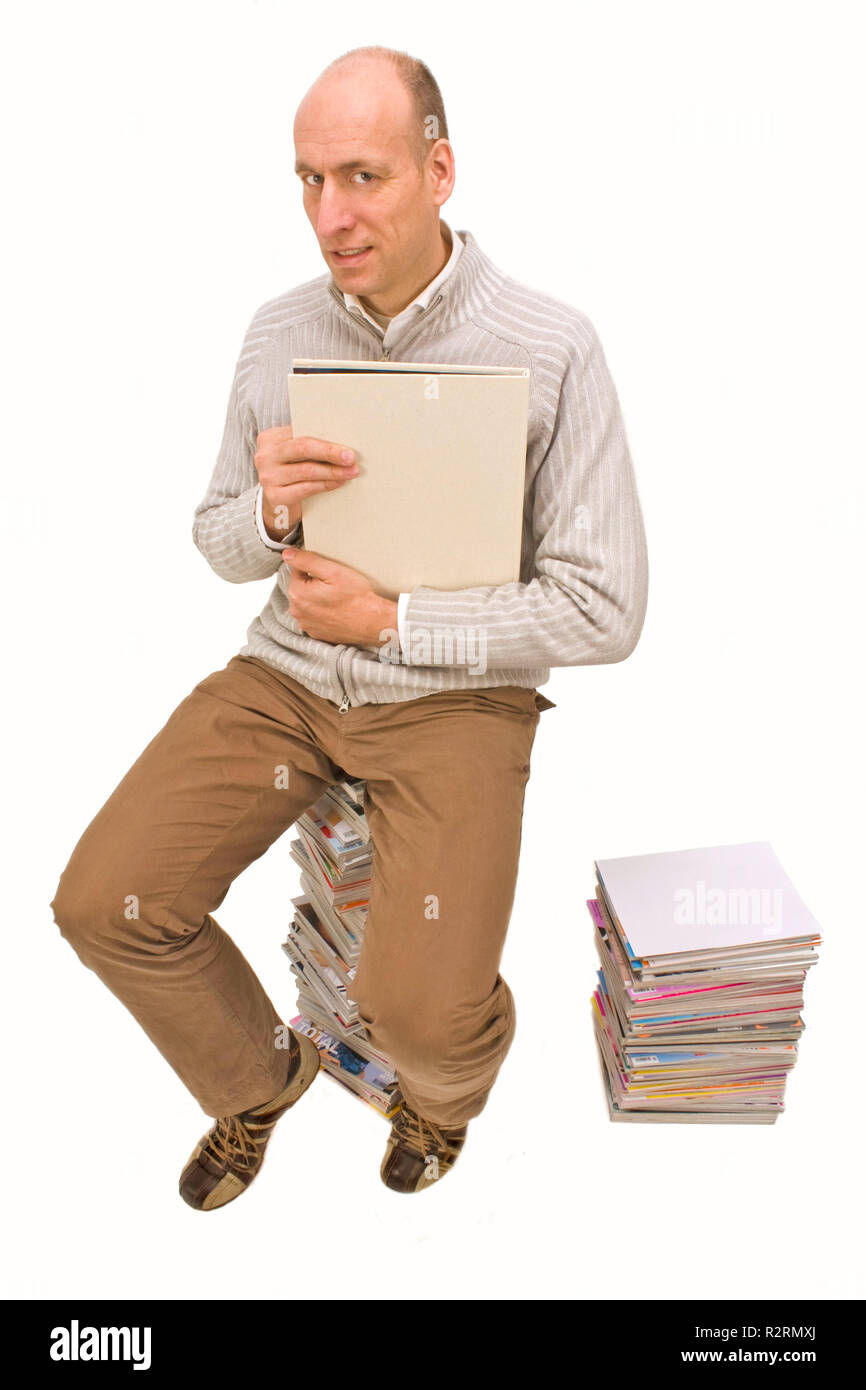 Homme assis sur une pile de magazines et en regardant un livre Banque D'Images