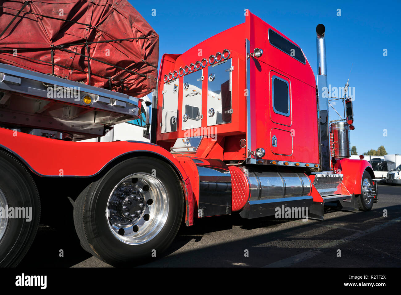 Gros camion rouge vif semi truck américain classique avec parties chromées et semi-remorque à plateau transporter du fret commercial couverts et fixée par les élingues sur socle Banque D'Images