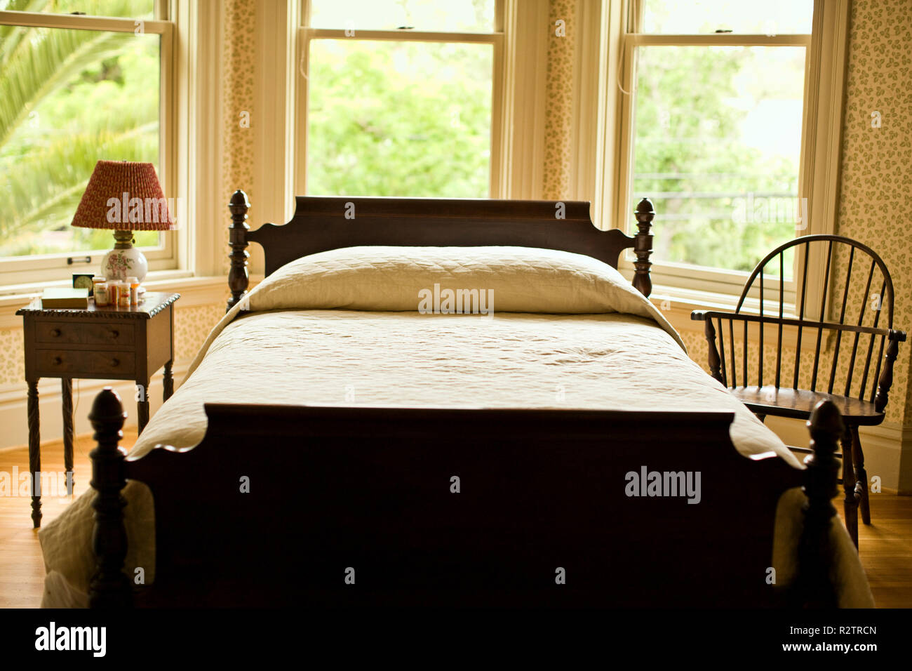 Lit en bois, table de chevet et une chaise dans une baie vitrée chambre à coucher. Banque D'Images