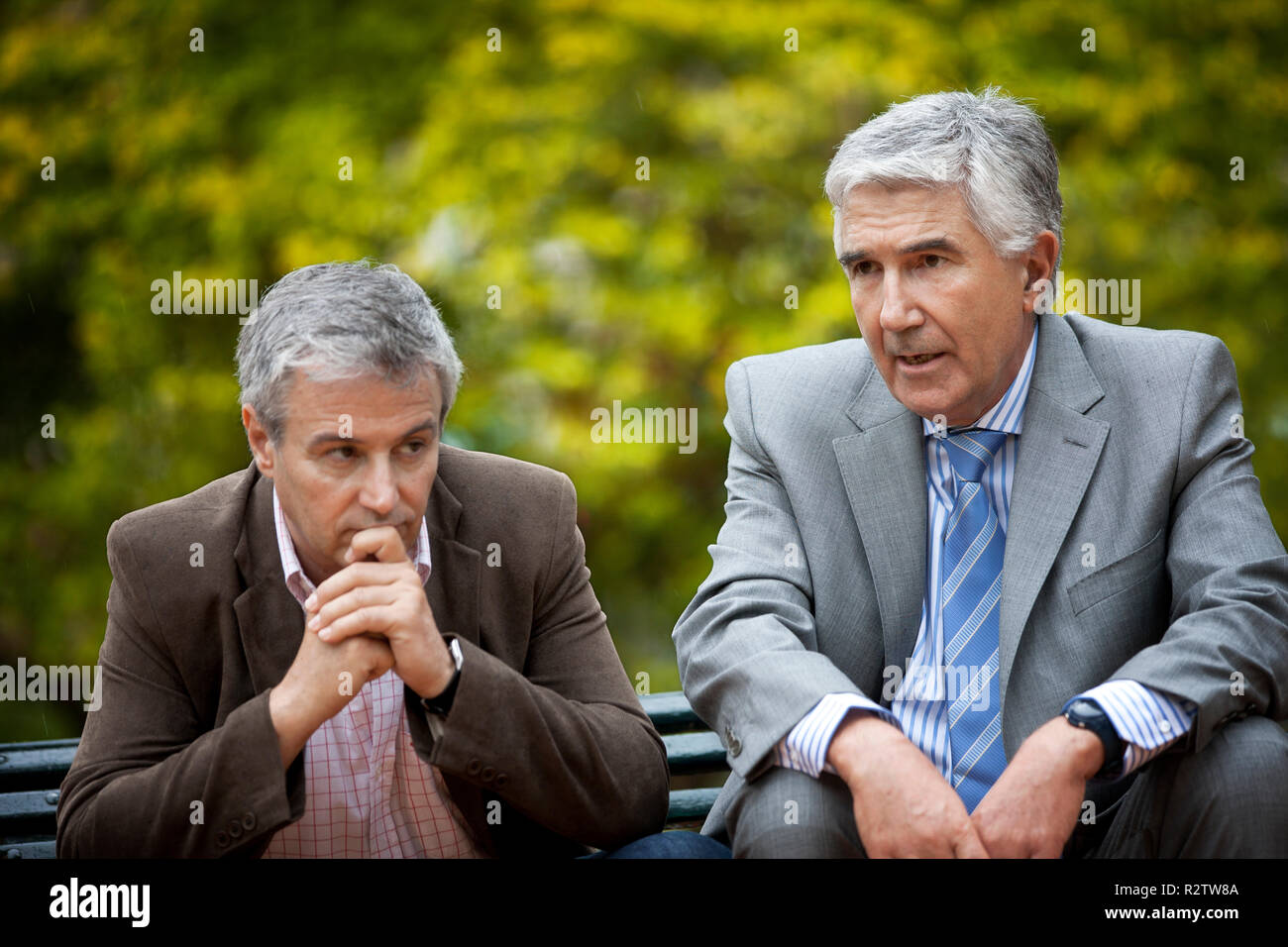 Deux hommes d'âge mûr parler sérieusement, assis ensemble sur un banc de parc. Banque D'Images