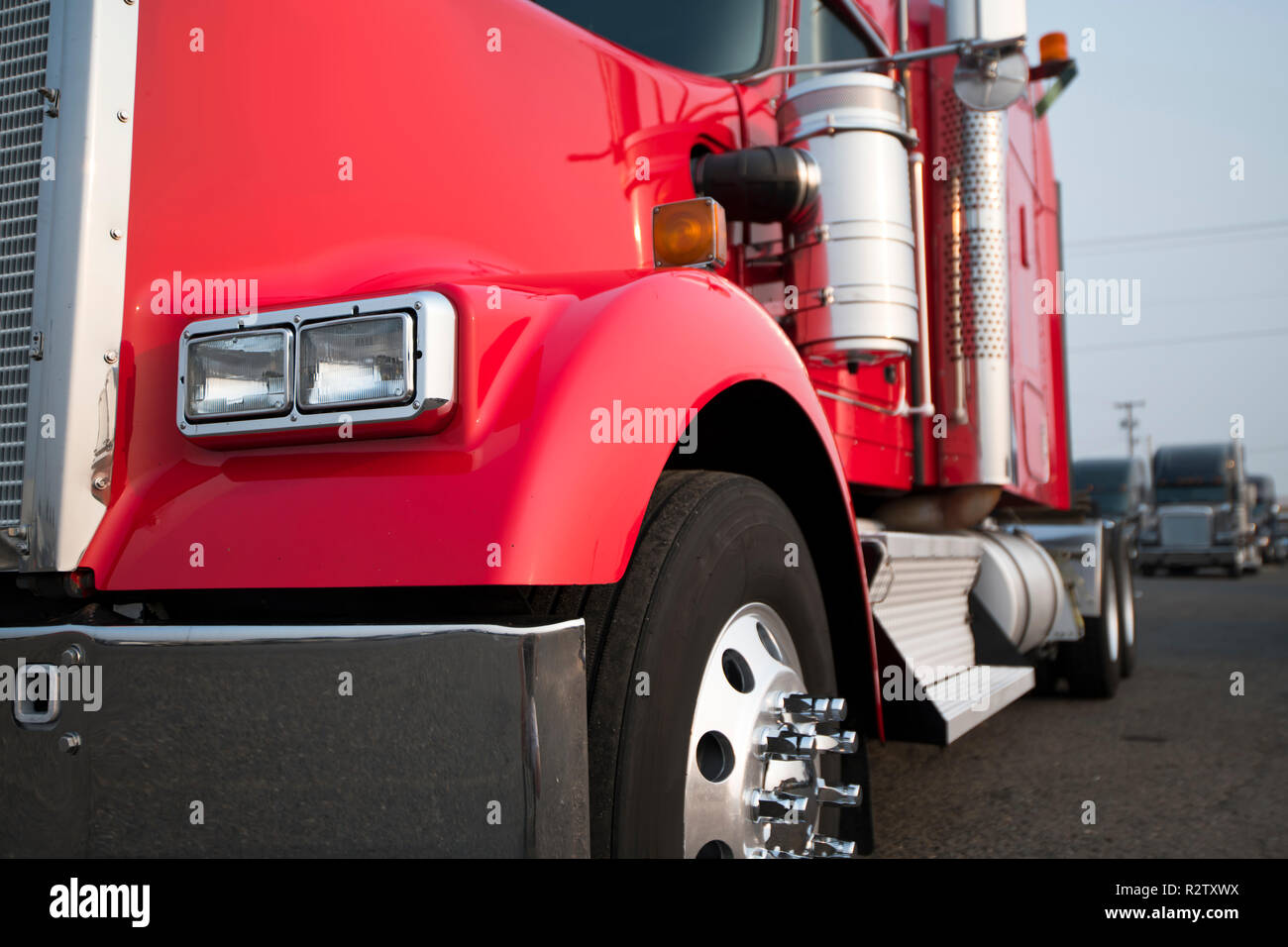 Gros camion rouge vif semi truck américain classique avec parties chromées et semi-remorque à plateau transporter la cargaison commerciale fixée par élingues sur truck stop Banque D'Images