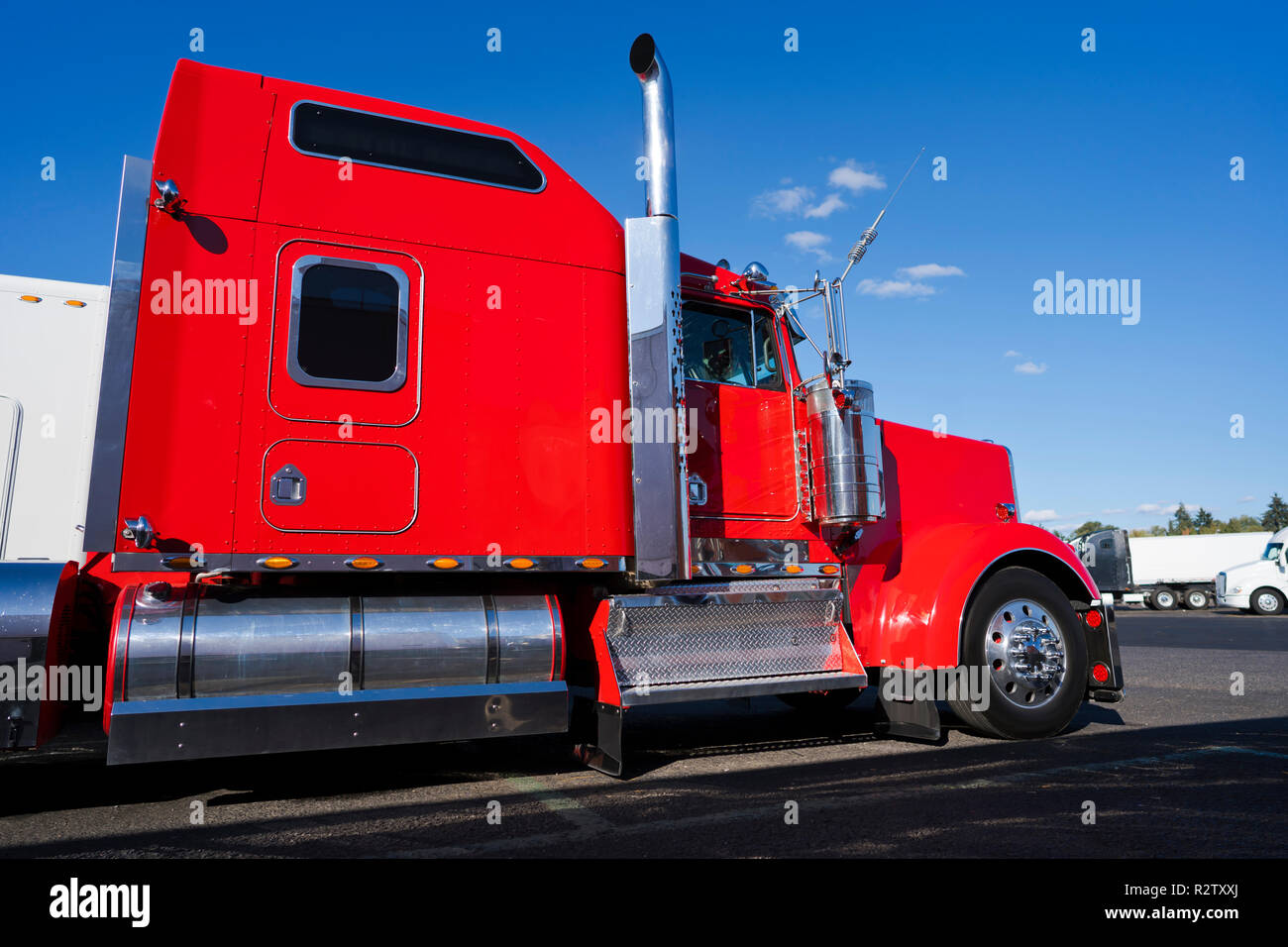 Profil de gros camion rouge vif semi truck américain classique avec parties chromées et semi-remorque à plateau transporter la cargaison commerciale fixée par élingues sur socle Banque D'Images