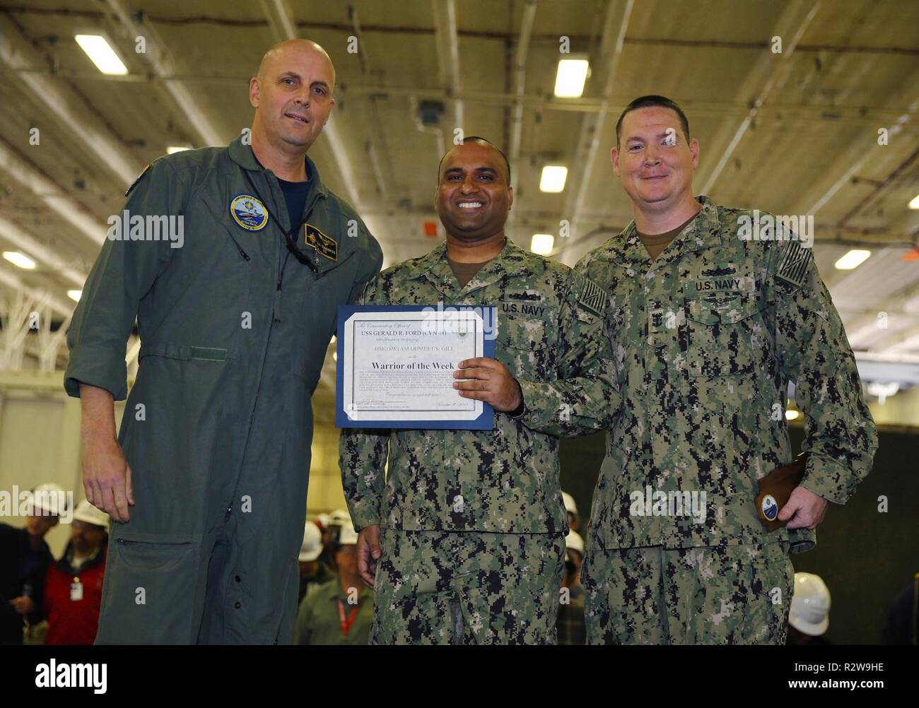 NEWPORT NEWS, Virginie (nov. 8, 2018), USS Gerald R. Ford (CVN 78) Commandant Capitaine John J. Cummings et Master Chief Operations Specialist Robert Laird Jr., posent pour une photo avec Ford's guerrier de la semaine, l'hôpital Corpsman 1re classe Amarpreet Gill, de New York, pendant un appel mains dans le hangar du navire. Ford est actuellement en post-shakedown la disponibilité de Huntington Ingalls Industries-Newport News Shipbuilding. Banque D'Images