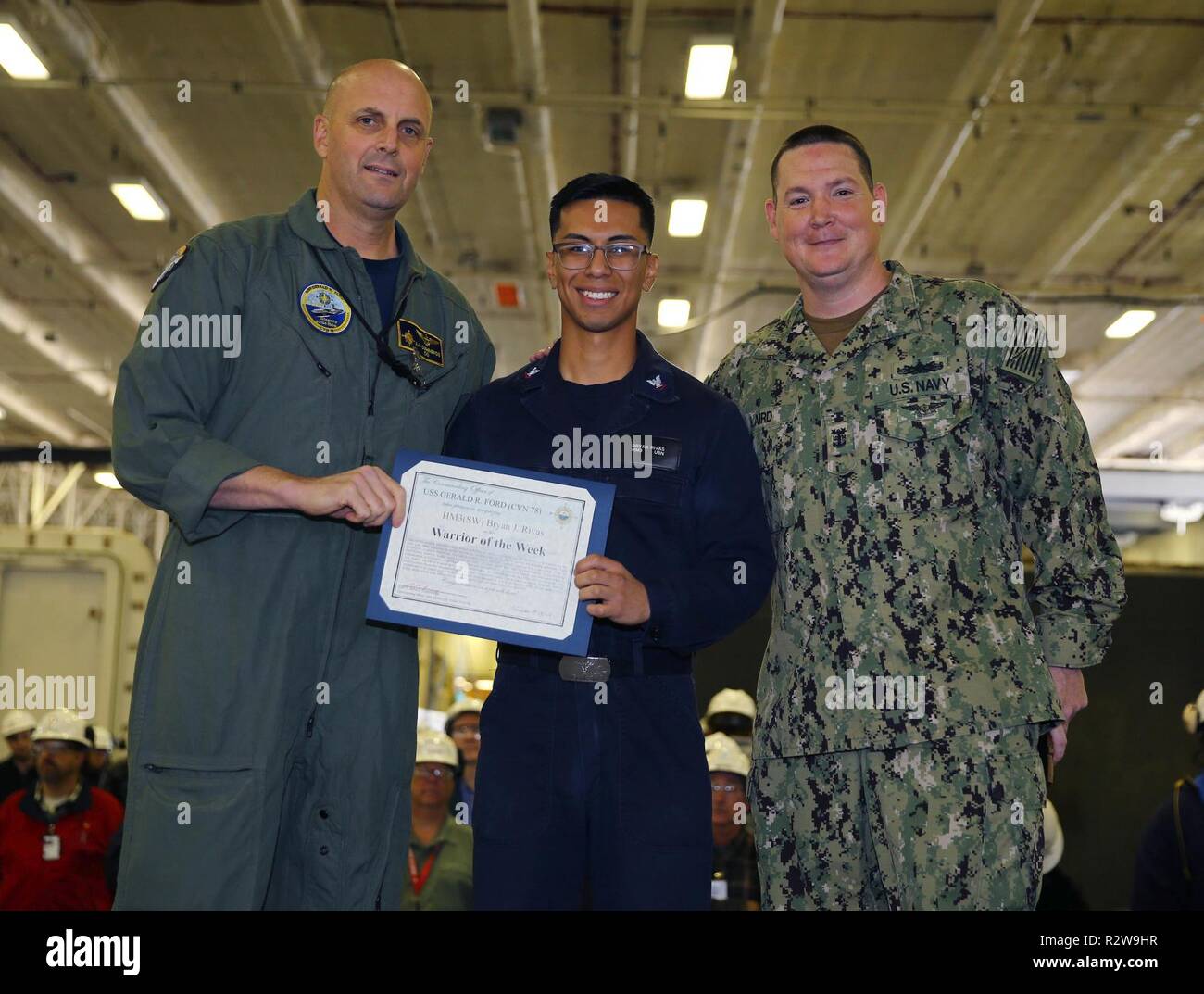 NEWPORT NEWS, Virginie (nov. 8, 2018), USS Gerald R. Ford (CVN 78) Commandant Capitaine John J. Cummings et Master Chief Operations Specialist Robert Laird Jr., posent pour une photo avec Ford's guerrier de la semaine, l'hôpital Corpsman 3rd Class Bryan Rivas, de Lehigh Acres, Florida, pendant un appel mains dans le hangar du navire. Ford est actuellement en post-shakedown la disponibilité de Huntington Ingalls Industries-Newport News Shipbuilding. Banque D'Images