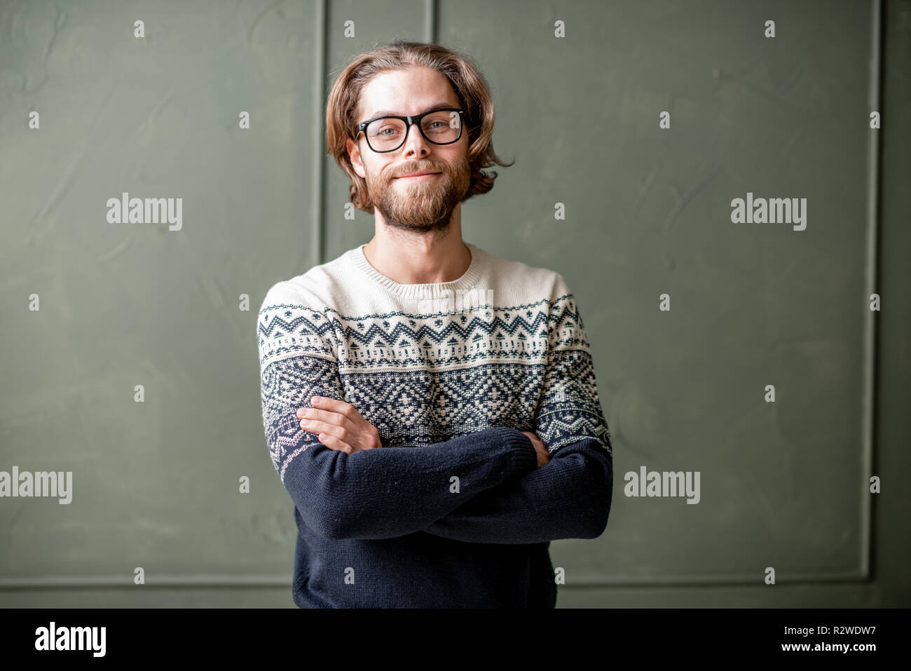 Portrait d'un jeune homme barbu aux cheveux longs vêtus de pull sur le mur à l'intérieur fond vert Banque D'Images