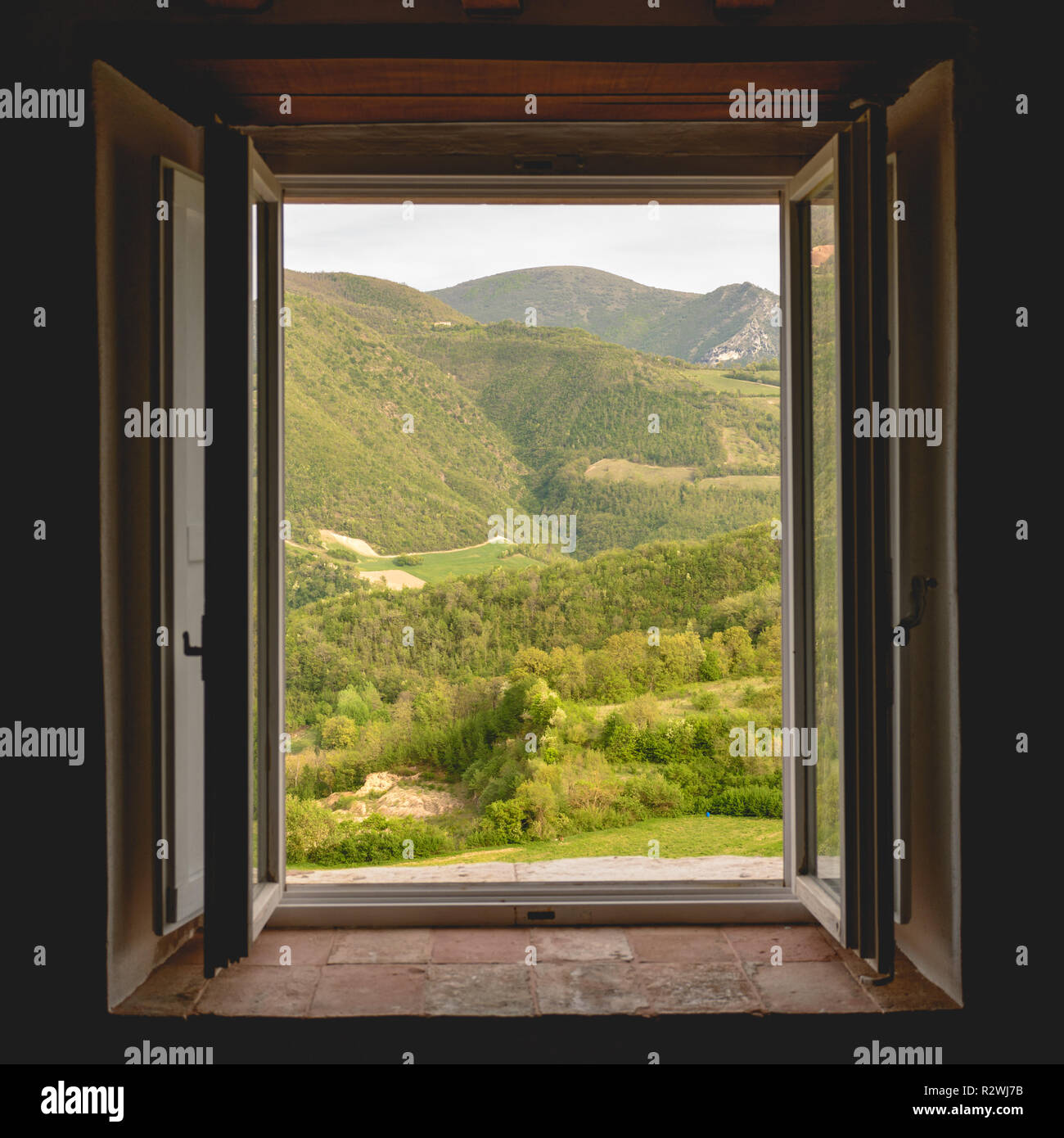 Vue sur une vallée verdoyante et les montagnes dans la région italienne de l'Ombrie à travers la fenêtre ouverte d'un bâtiment rural. Format carré. Banque D'Images
