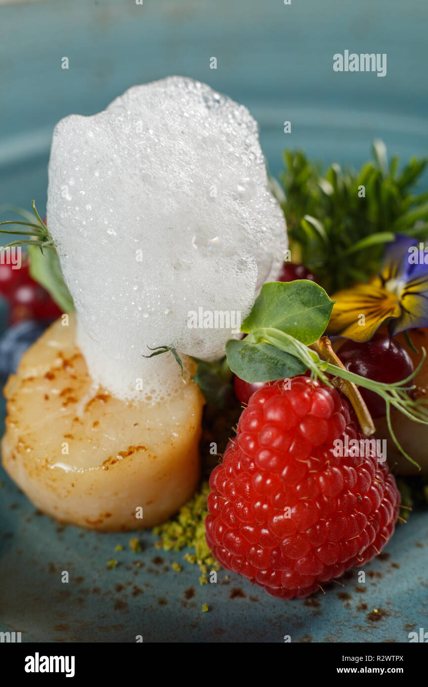 Poires poêlées sur un lit de pistaches au sol, garni de mousse d'oeufs sur une plaque bleue Banque D'Images