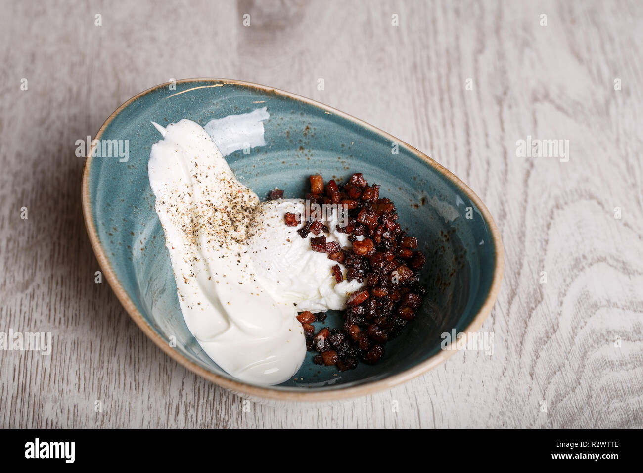 Oeufs durs avec lard grillé et la crème sure dans un bol bleu Banque D'Images