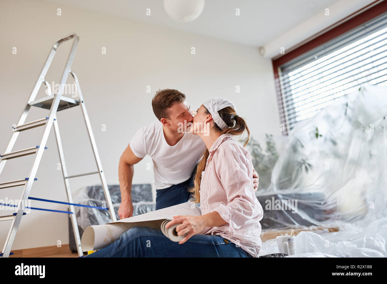 Happy young couple embrasse tout en papier peint et peinture in new home Banque D'Images