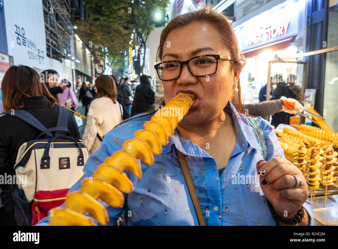 Une dame mange une pomme de terre de feu sur une spirale stick acheté forment un street food à Gangnam de Séoul, en Corée du Sud. Banque D'Images