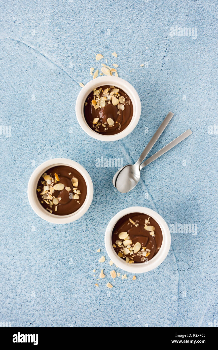Pudding au chocolat maison dans trois ramequins et cuillères à café en céramique blanche sur fond bleu clair avec copie espace concret. Vue d'en haut. Banque D'Images