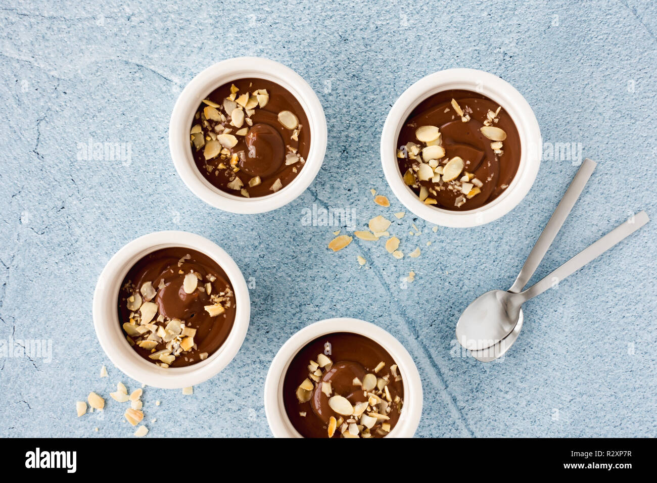Pudding au chocolat maison dans trois ramequins en céramique blanche avec des amandes effilées grillées et de cuillères à café bleu clair sur fond de béton. Vue d'en haut. Banque D'Images