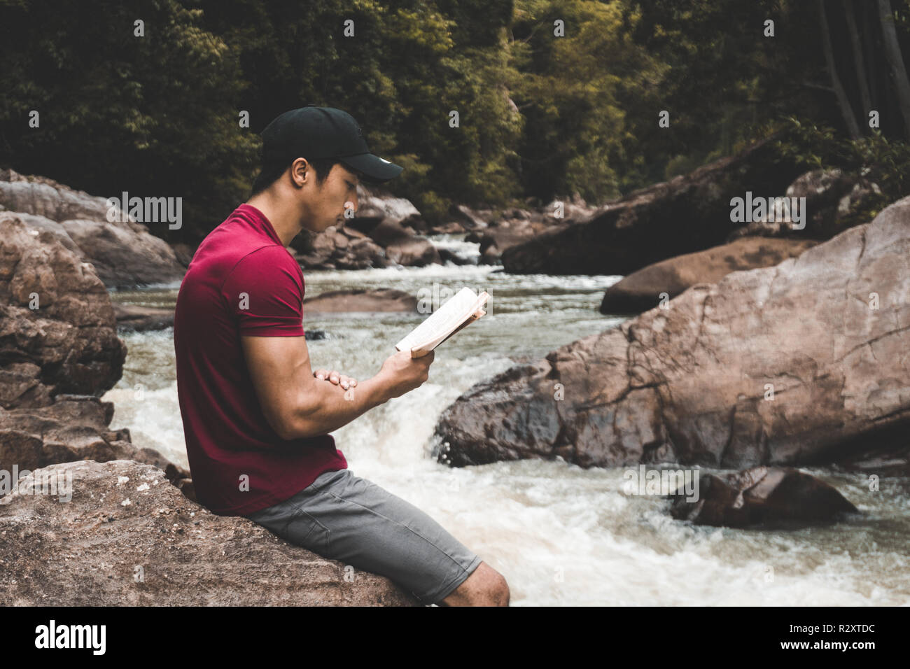 Man relaxing in the woods tout en lisant un livre près d'une rivière dans la nature Banque D'Images