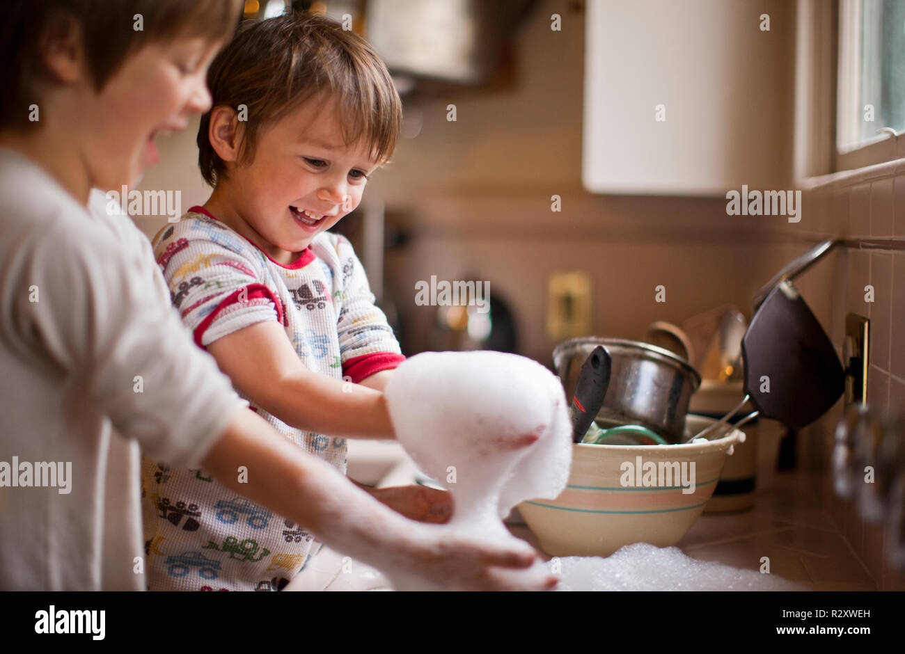 Deux frères jouant avec de l'eau savonneuse pendant le lavage. Banque D'Images