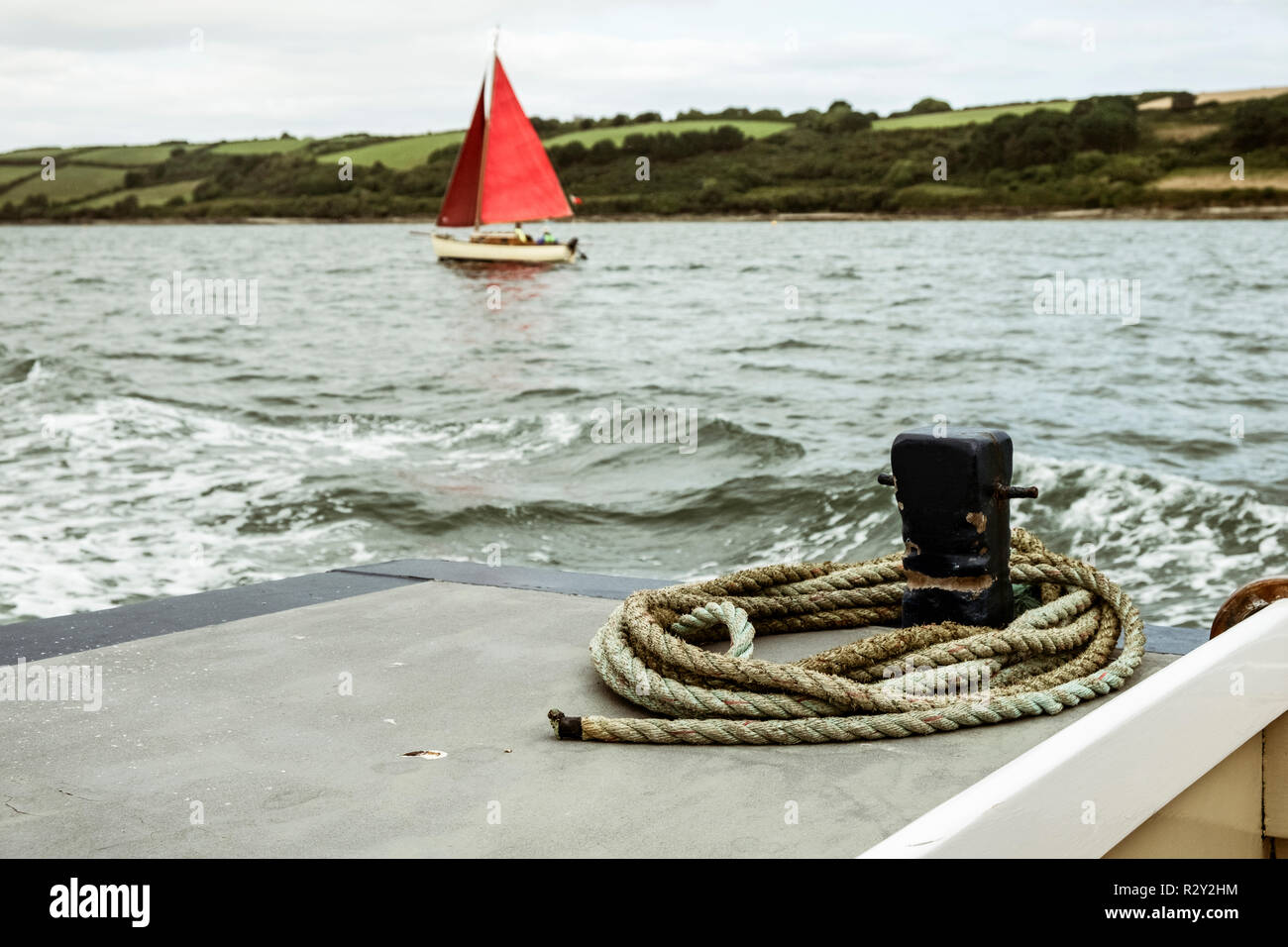 Un bateau à voile avec voiles rouge vif sur l'eau, vu d'un autre bateau. Banque D'Images